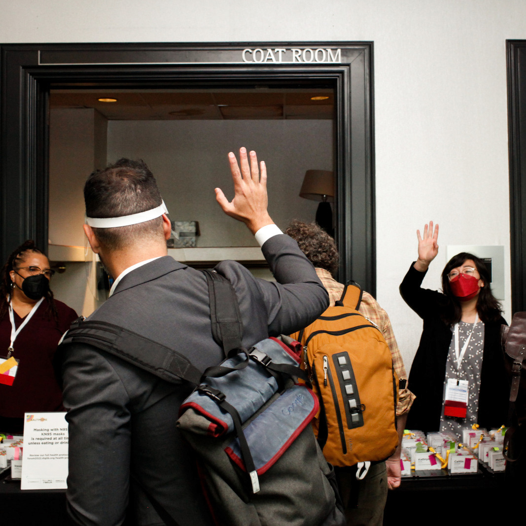 CLIR staff member standing at 2022 DLF Forum registration table, waving to a man wearing a backpack with his back to the camera